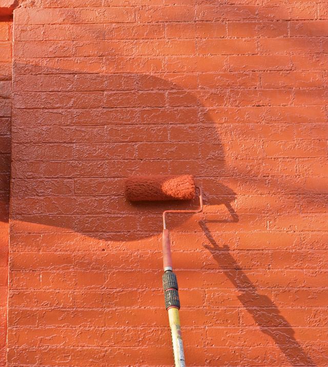 Een verfroller zet een bakstenen muur in het oranje